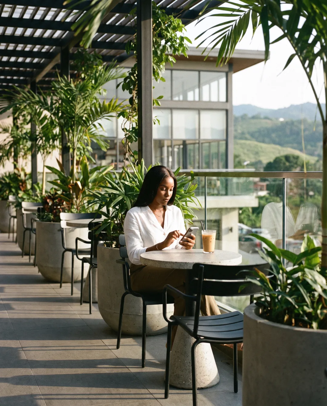 Customer scrolling a social feed on her phone at a cafe terrace in Port of Spain